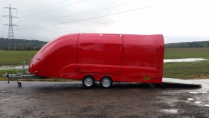 Red enclosed vehicle trailer on the side of the road next to a flooded field