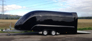 Black enclosed trailer with the rear hatch lowered on the side of the road next to a field