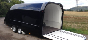 Black enclosed trailer with the rear hatch lowered on the side of the road next to a field