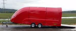 Red enclosed vehicle trailer on the side of the road next to a flooded field