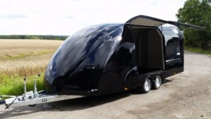 Black enclosed vehicle trailer on the side of the road with the side hatch open next to a field