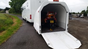 Orange bike inside a white enclosed motorbike trailer attached to a white motorhome