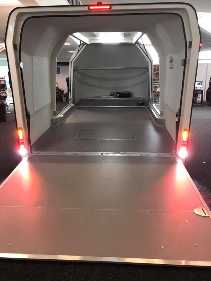 Enclosed vehicle trailer inside a workshop with all the doors open and with the rear lights illuminated