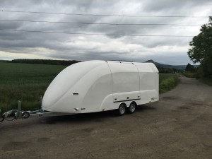 White enclosed vehicle trailer in front of a large field on the side of the road