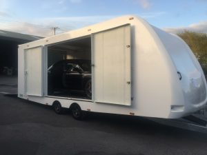 Black sports car inside a white vehicle trailer with the side doors open
