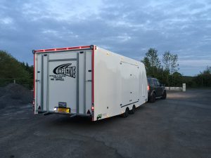 Large white enclosed vehicle trailer in a concrete yard attached to a land rover