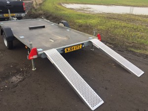 Grey flatbed trailer with ramps down in front of a field
