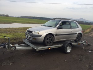 Silver Citroen Saxo on a grey flatbed trailer in front of a field