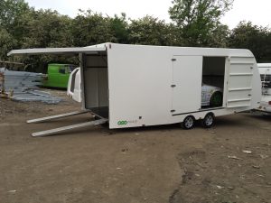 Side of a white enclosed vehicle trailer with the rear hatch and side door open with a white BMW 3 series compact in
