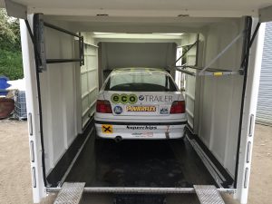 White BMW 3 series compact track car with sponsors on the rear inside a white enclosed trailer
