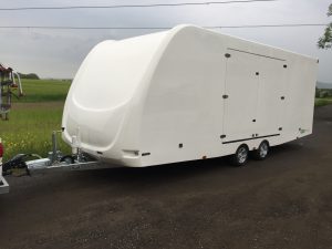 Large white vehicle trailer on the side of the road next to a field