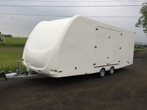 Large white vehicle trailer on the side of the road next to a field
