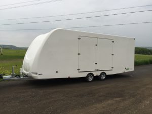 Side of a large enclosed vehicle trailer in front of a field on the side of the road