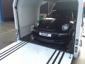 Porsche 911 cup car in the back of a white enclosed vehicle trailer