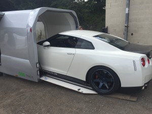 White Nissan GTR being loaded onto a silver vehicle trailer