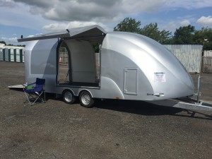 Silver enclosed vehicle trailer with hatches open in a gravel yard