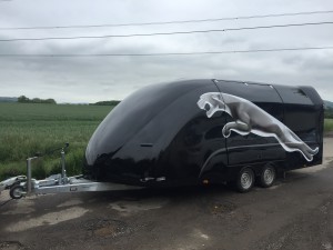 Black vehicle trailer with a large Jaguar logo on the side in front of a field