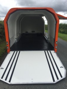 Orange trailer with the white rear hatch down with black stripes on