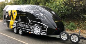 Black enclosed vehicle trailer with white and yellow decals on the side
