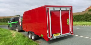 Red enclosed vehicle trailer at the side of the road attached to a grey transit van