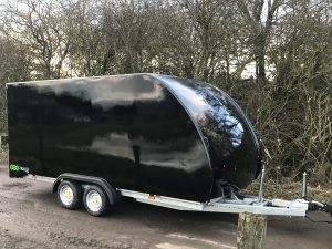 Black enclosed vehicle trailer at the side of the road next to trees