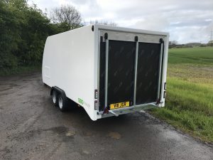 Small white enclosed vehicle trailer on the side of the road next to a field