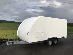 White enclosed vehicle trailer on the side of the road next to a field