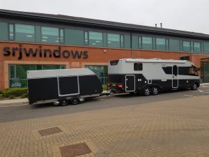Black and silver trailer attached to a large motorhome with teh same colour scheme in front of a large building