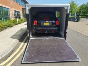 Black Mini Cooper S JCW in a silver and black trailer with the side door and ramp open