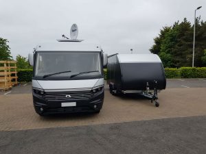 Black and silver vehicle trailer in a car park next to a motor home with the same colour scheme