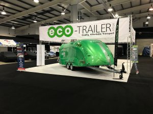Green enclosed vehicle trailer at an expo with a banner above it