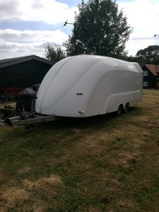 White enclosed vehicle trailer on a field in front of houses