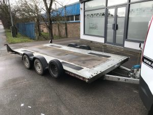 Silver flat bed trailer attached to a van in a carpark