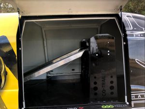 Silver and black vehicle ramp inside a black and yellow enclosed vehicle trailer with the side door open