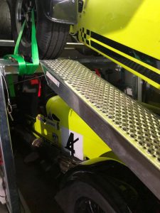 Two yellow caterhams in a black enclosed vehicle trailer with one on a ramp