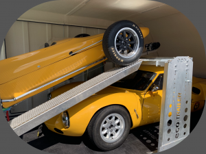 two yellow cars in a enclosed trailer with one on a ramp