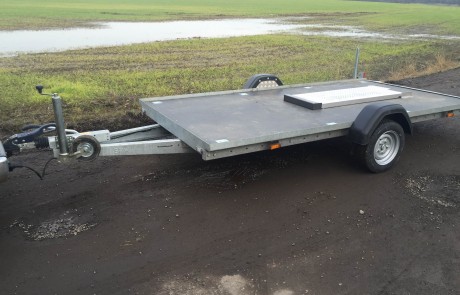 Silver flat bed trailer on a worn out road next to a field