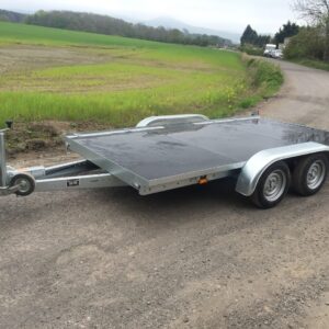 Silver flat bed trailer with a black bed on a gravel road