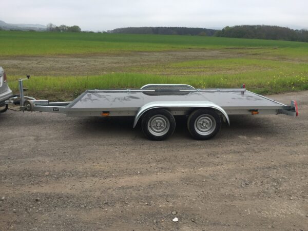 Silver flat bed trailer with a black bed on a gravel road