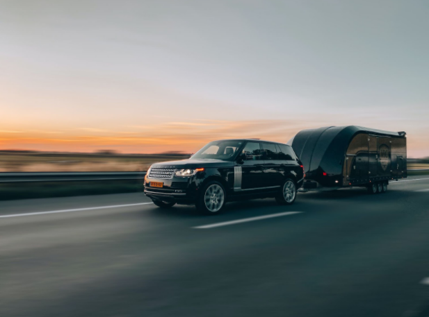 Black Range rover Sport pulling a black enclosed trailer on a motorway in front of a sunset